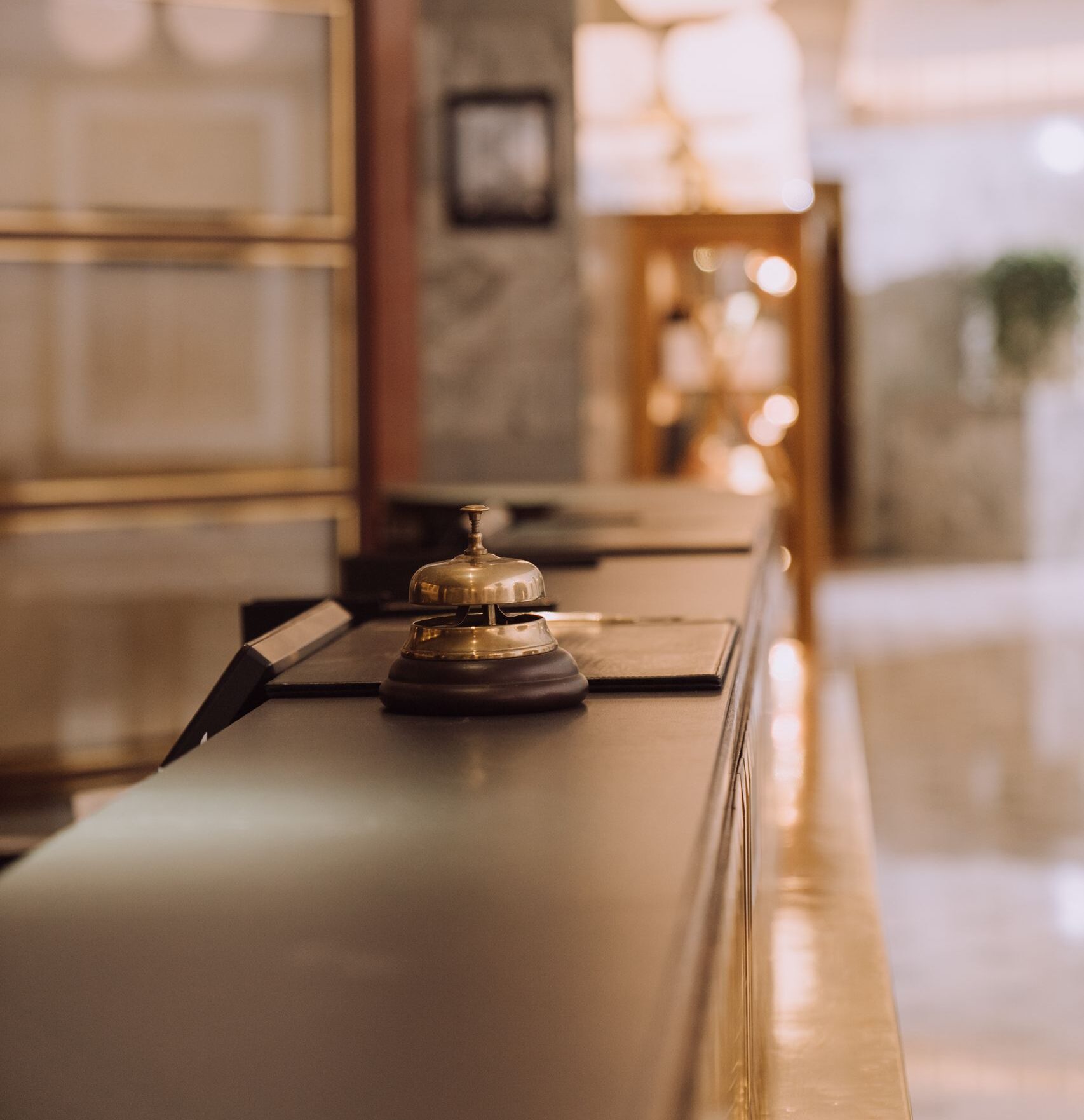 A close-up view of a hotel reception counter with a classic bell and warm lighting.